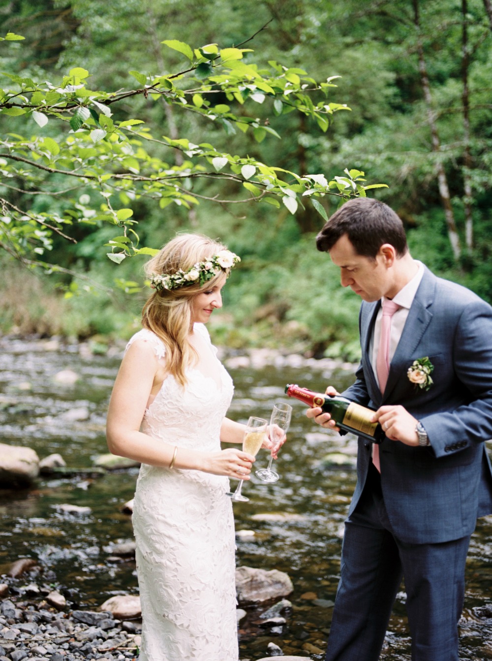 Bride and groom toasting champagne by a river