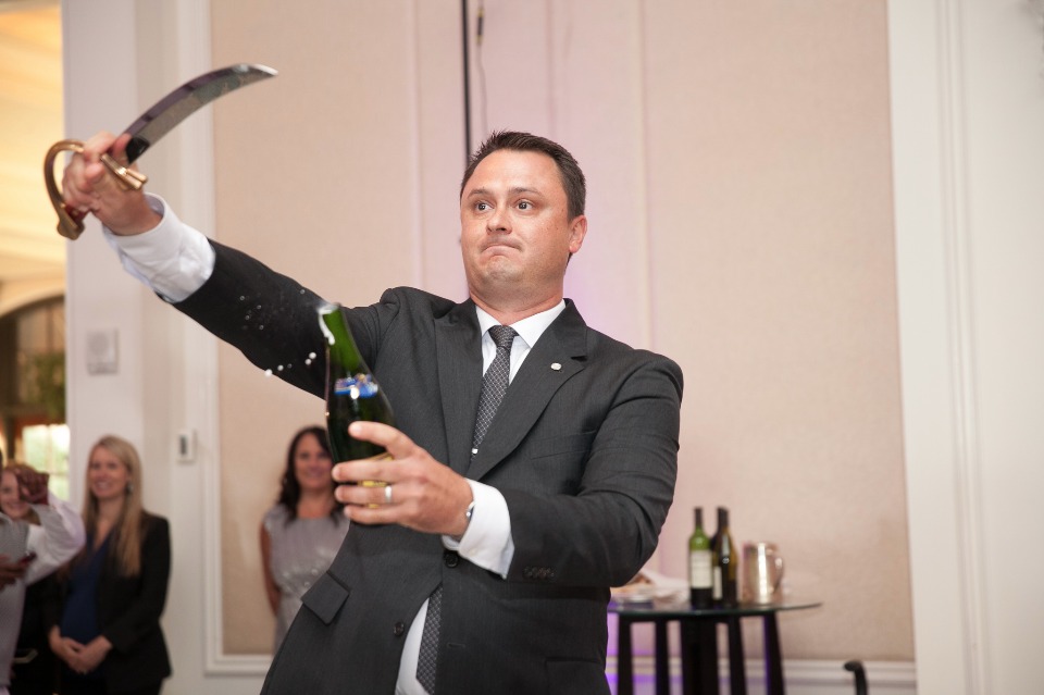 Man in suit sabering champagne bottle at event
