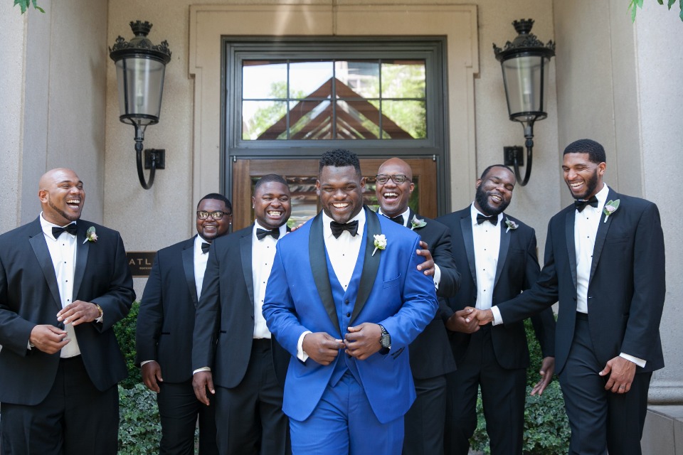 Groom and groomsmen laugh in tuxedos on wedding day