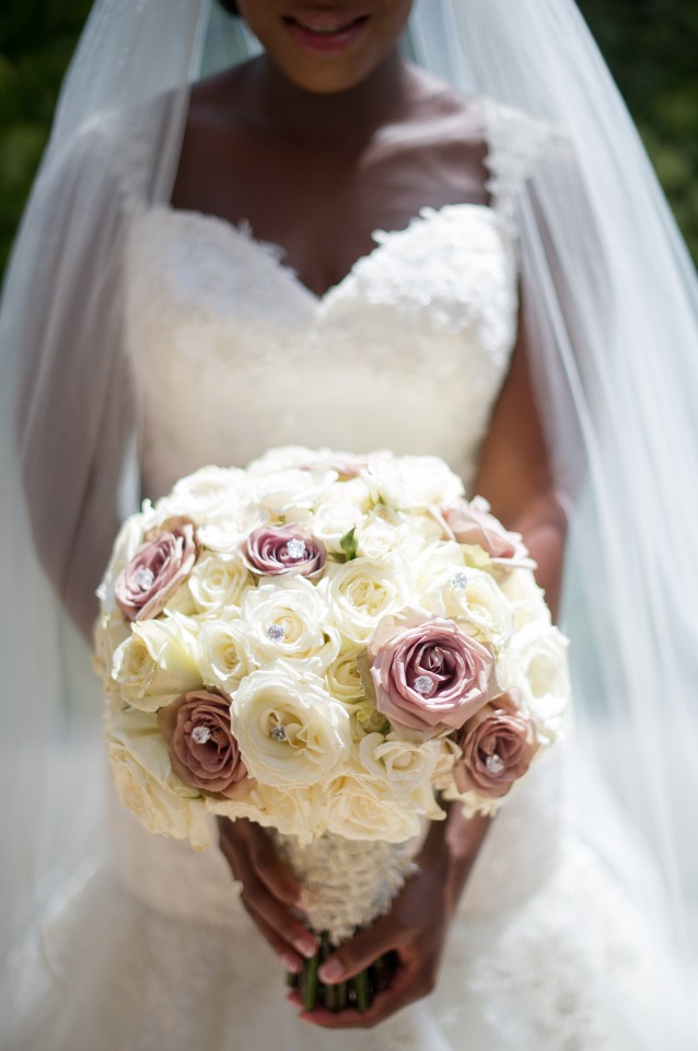 Bride in white dress holds rose and cream wedding bouquet