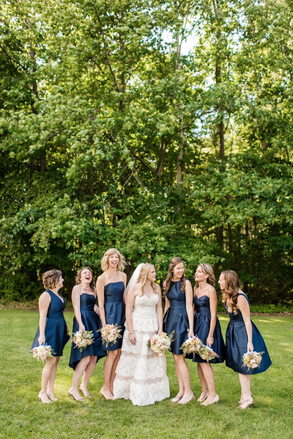Bride and bridesmaids in navy dresses smiling outdoors