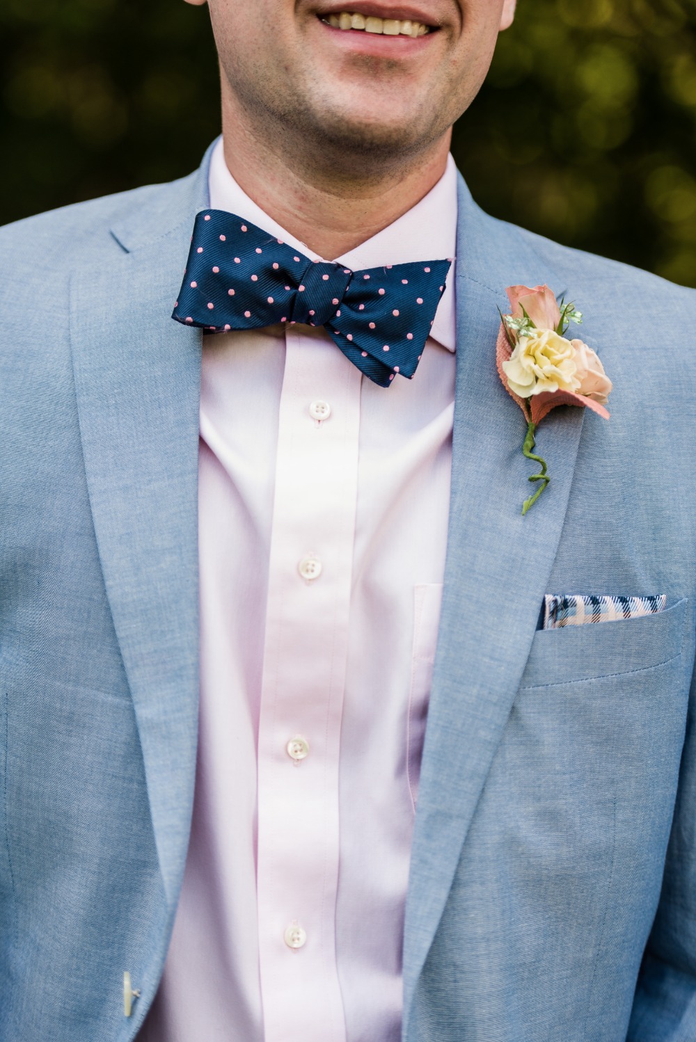 Man in light blue suit with navy polka dot bow tie and boutonniere
