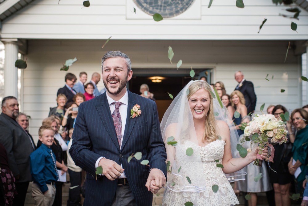 Cheerful newlyweds exit wedding showered with leaves