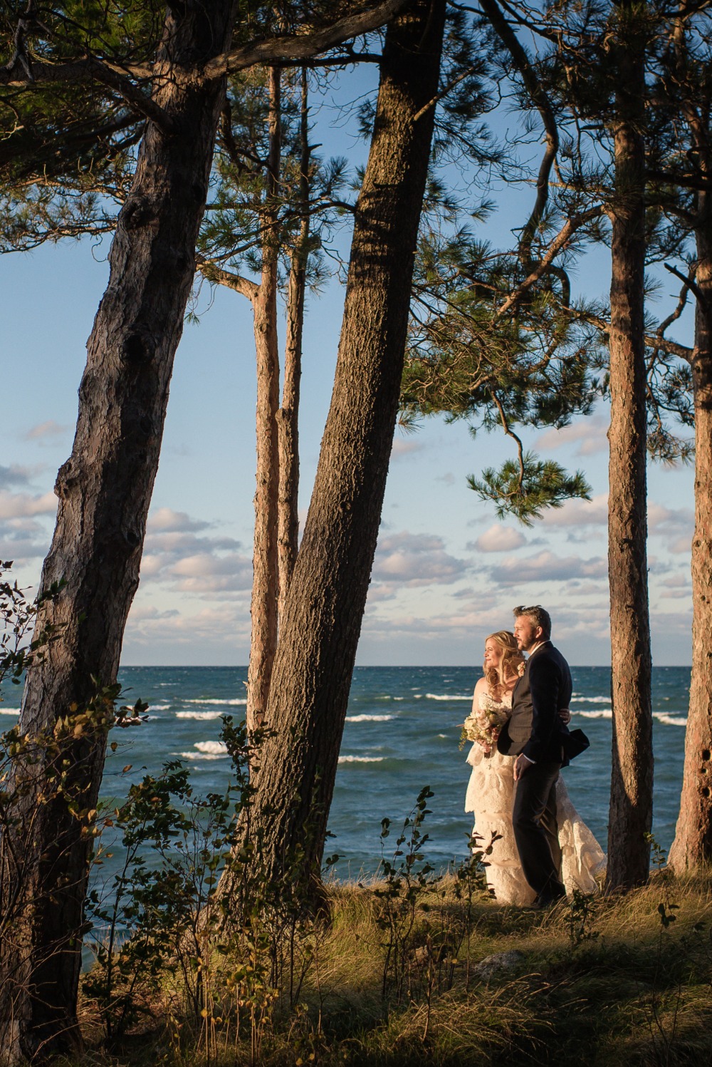 Bride and groom on ocean beach framed by tall trees