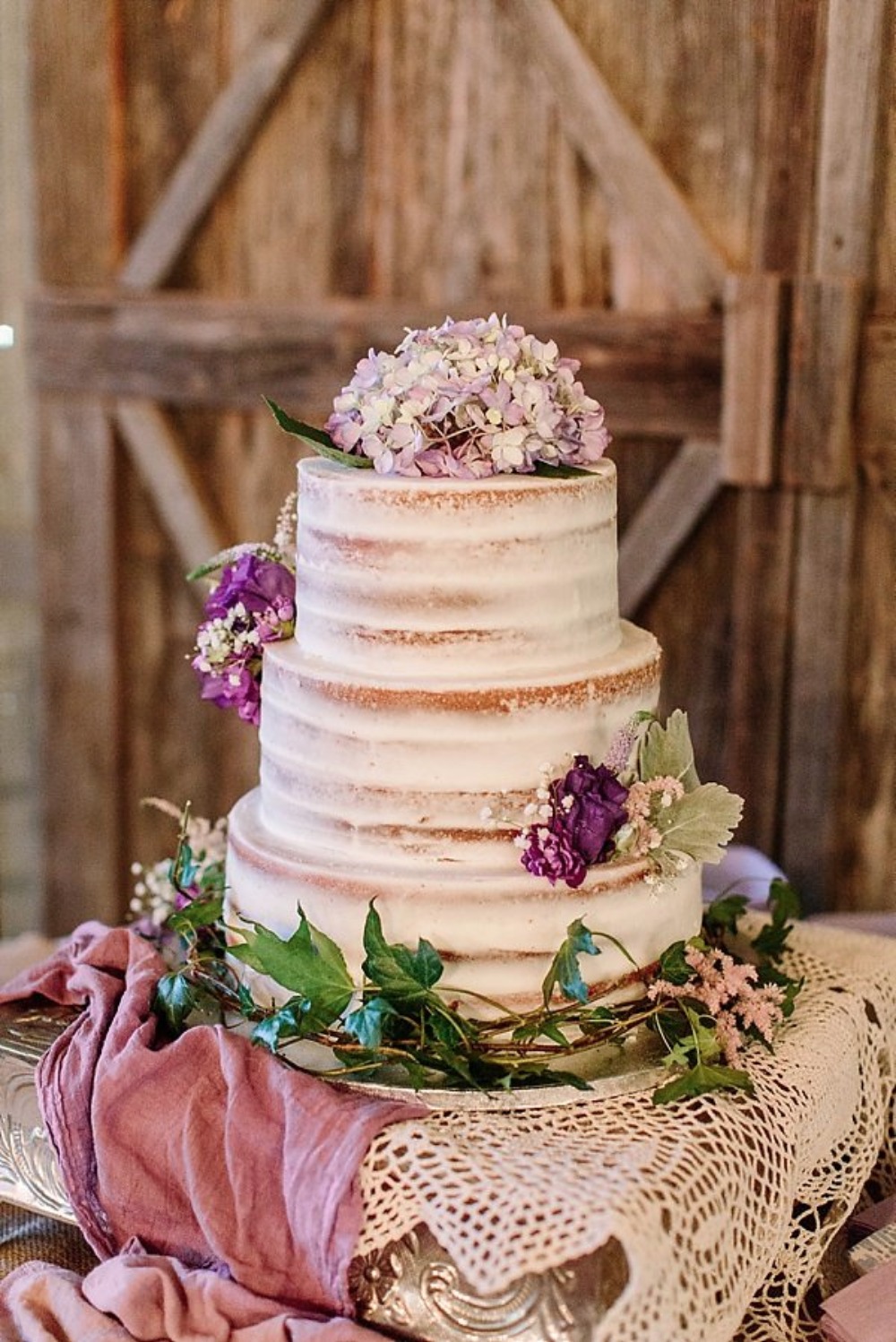 nearly naked wedding cake with purple flower topper