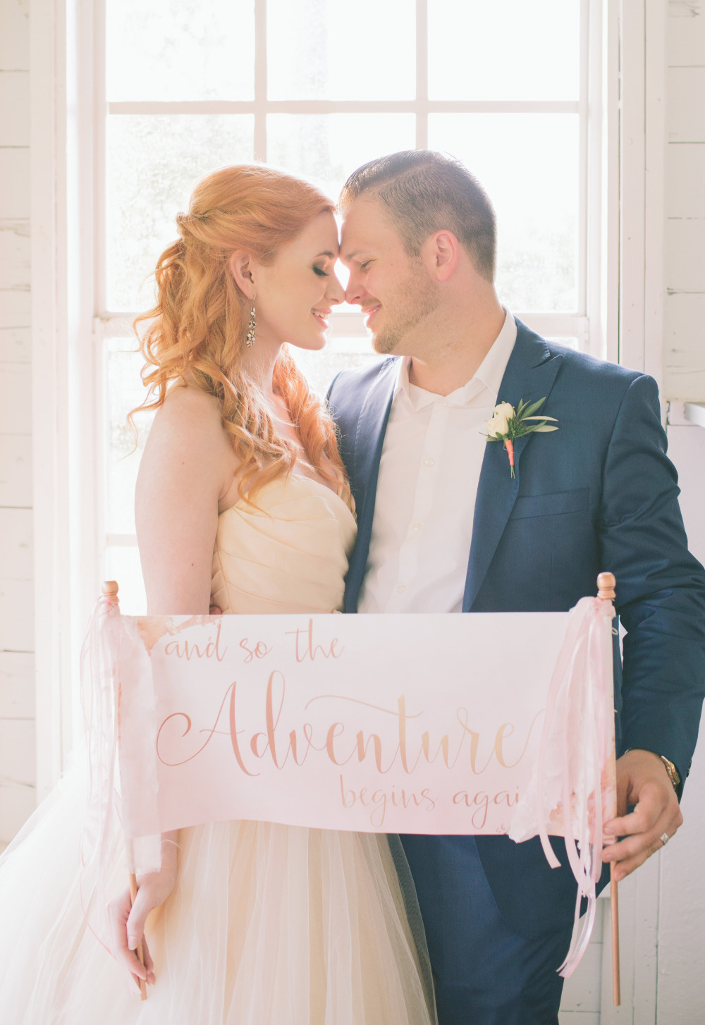 Newlywed couple holding And so the Adventure begins again sign