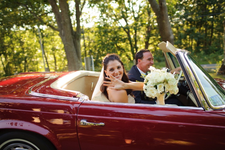bride and groom ride off in a cherry red classic convertable