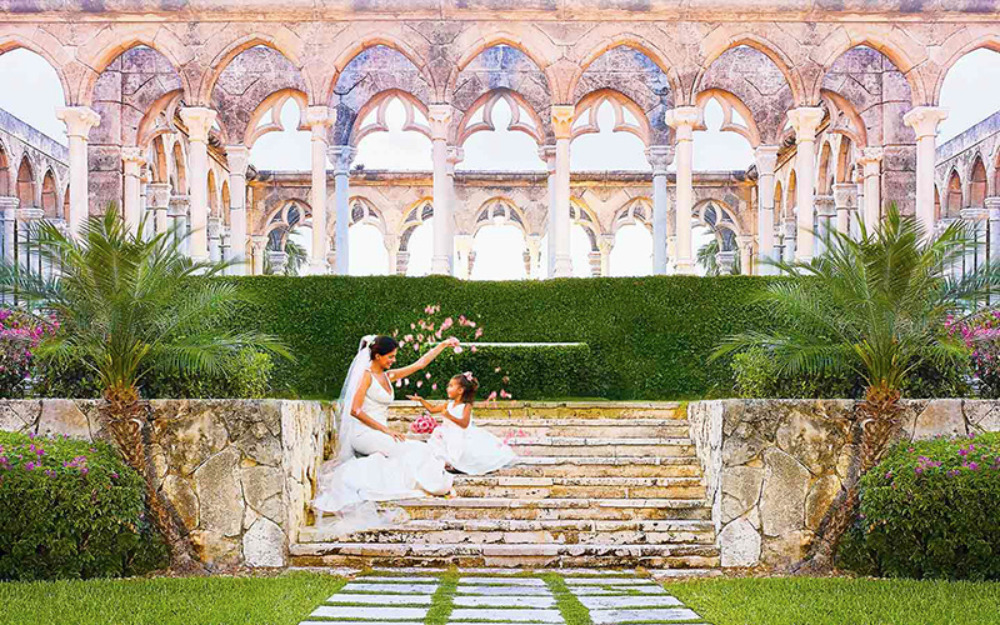 Bride and flower girl pose on steps before arched stone building