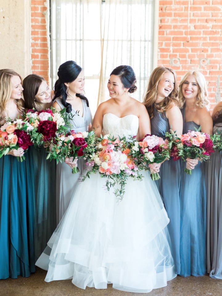 bridesmaids in assorted blue dresses with peach and deep red bouquets