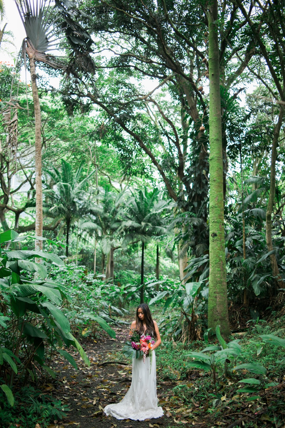 Bride in white dress holding bouquet in lush green forest