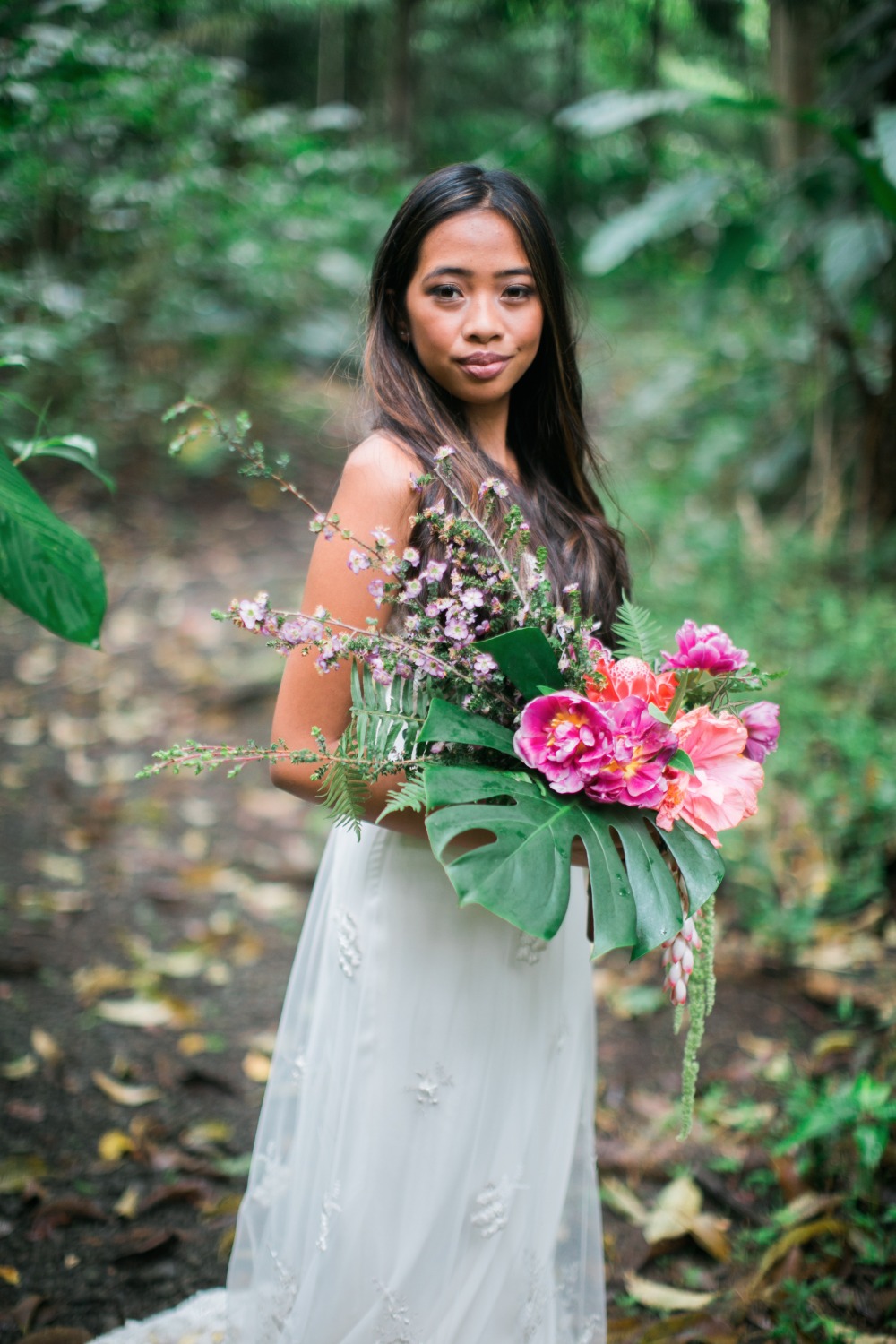 Smiling bride holding tropical flowers in forest setting