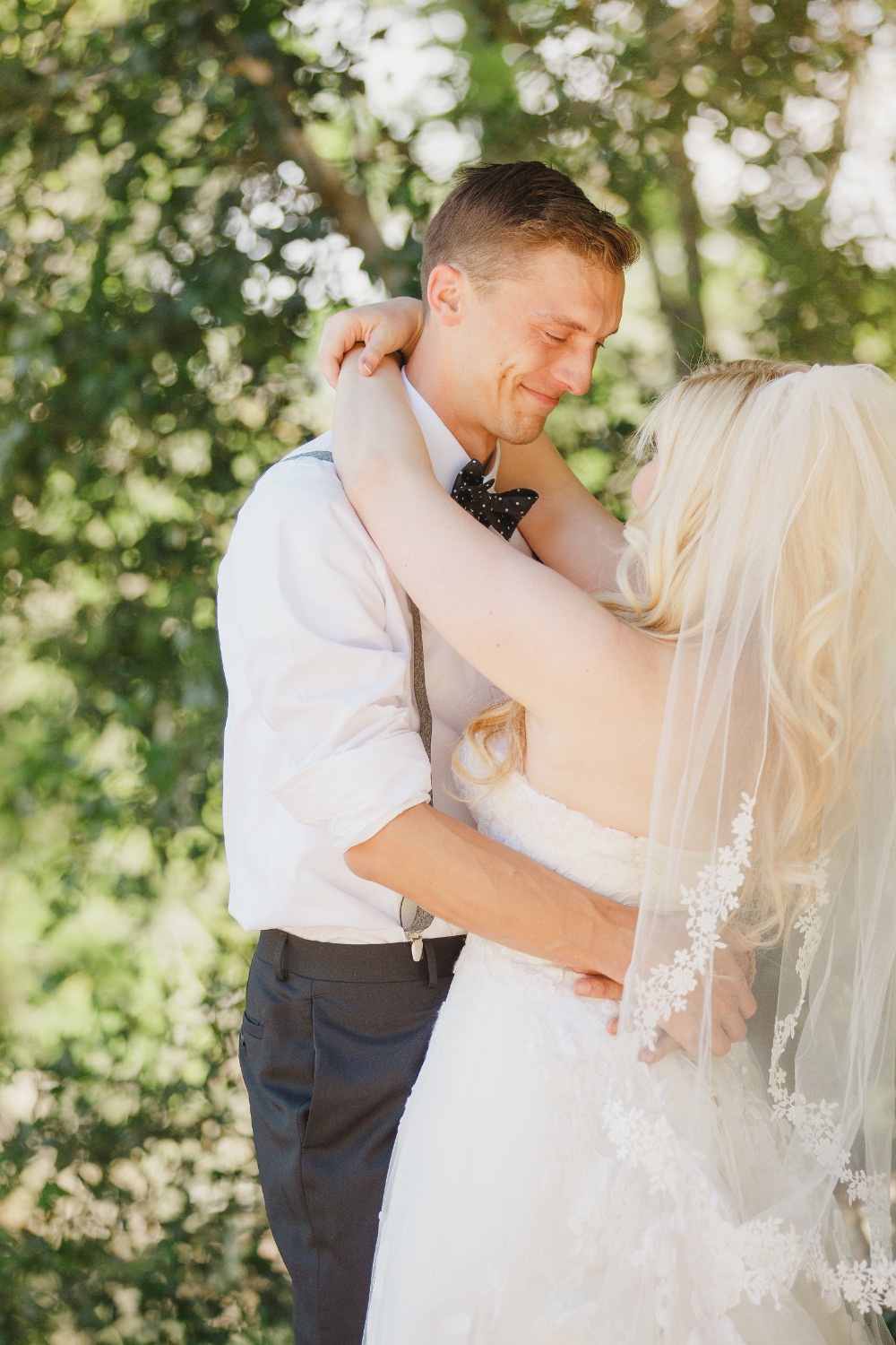 Groom smiles embracing bride outdoor wedding portrait