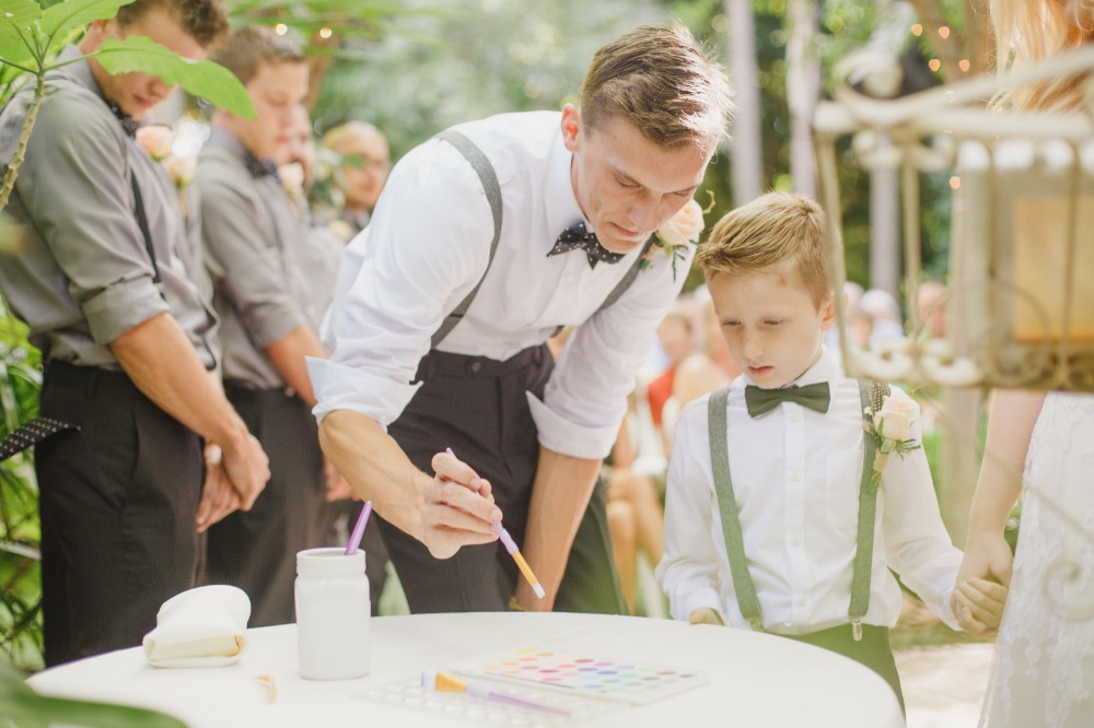 Groom and boy pour sand at outdoor wedding ceremony