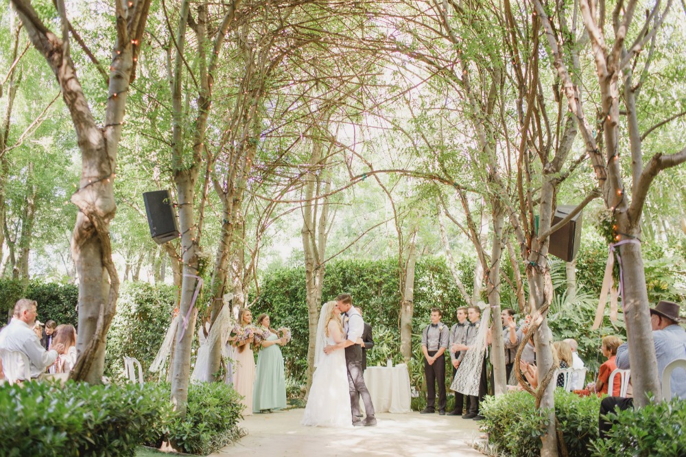 Outdoor wedding ceremony with a kiss under the tree canopy