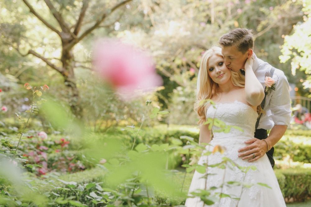 Couple in wedding attire embracing in a garden filled with flowers