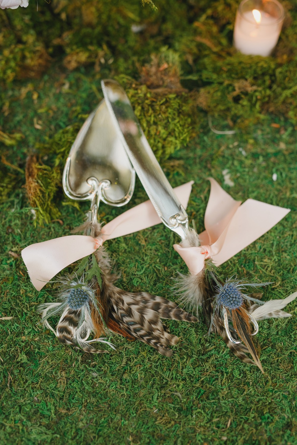 Cake servers with feather accents on moss for a wedding