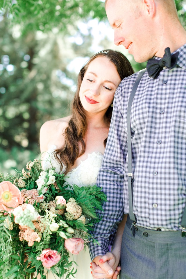 Bride rests head on groom holding bouquet outdoors