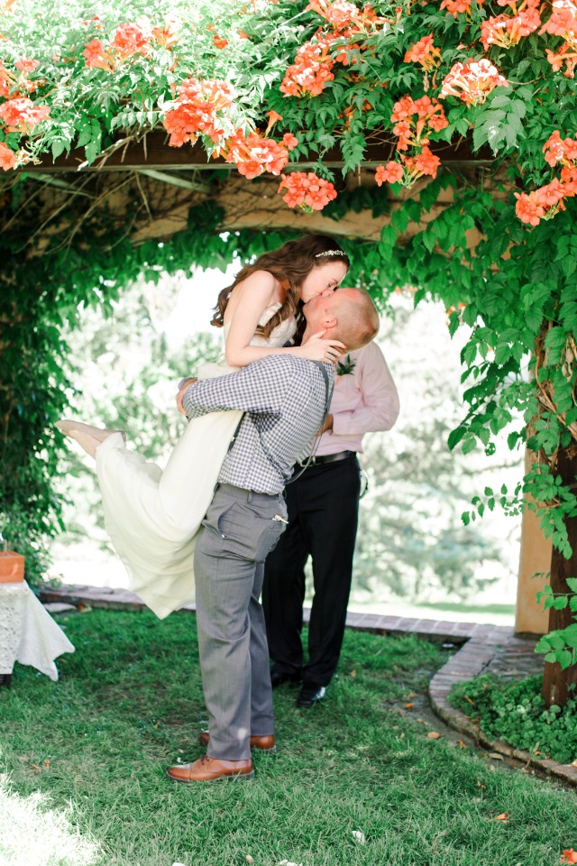 Groom lifts bride and kisses her under flower arch