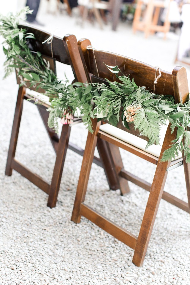 Wooden chairs decorated with greenery for an outdoor wedding ceremony
