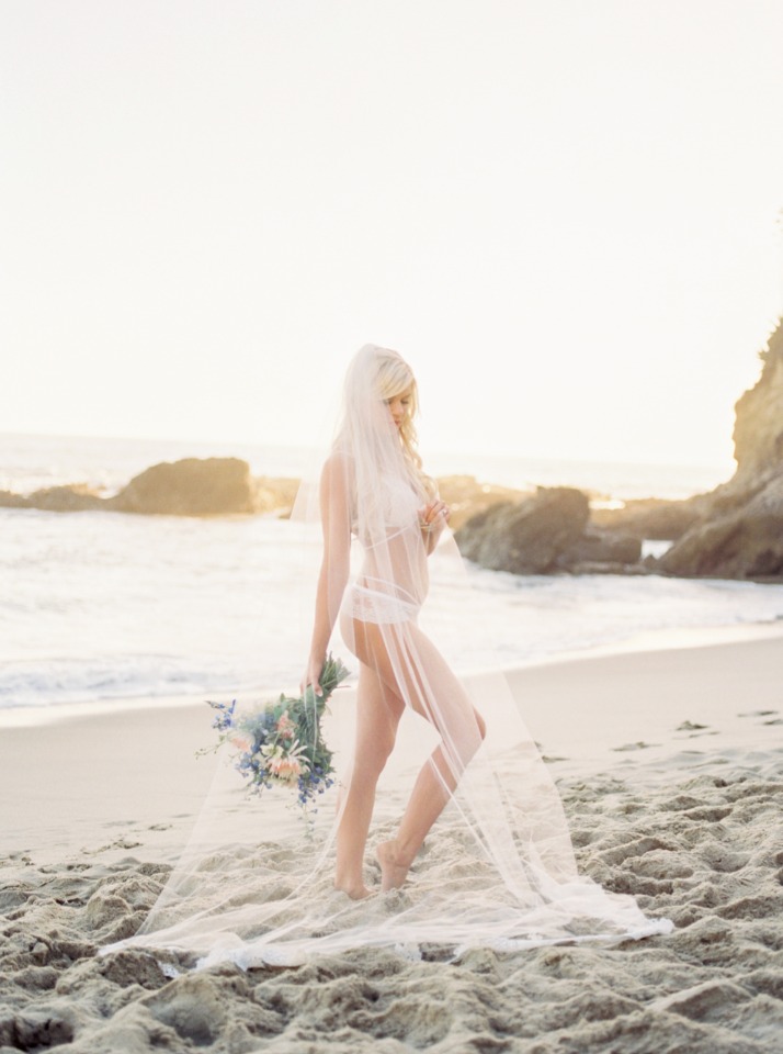 Beach bride in veil holding bouquet at ocean sunset