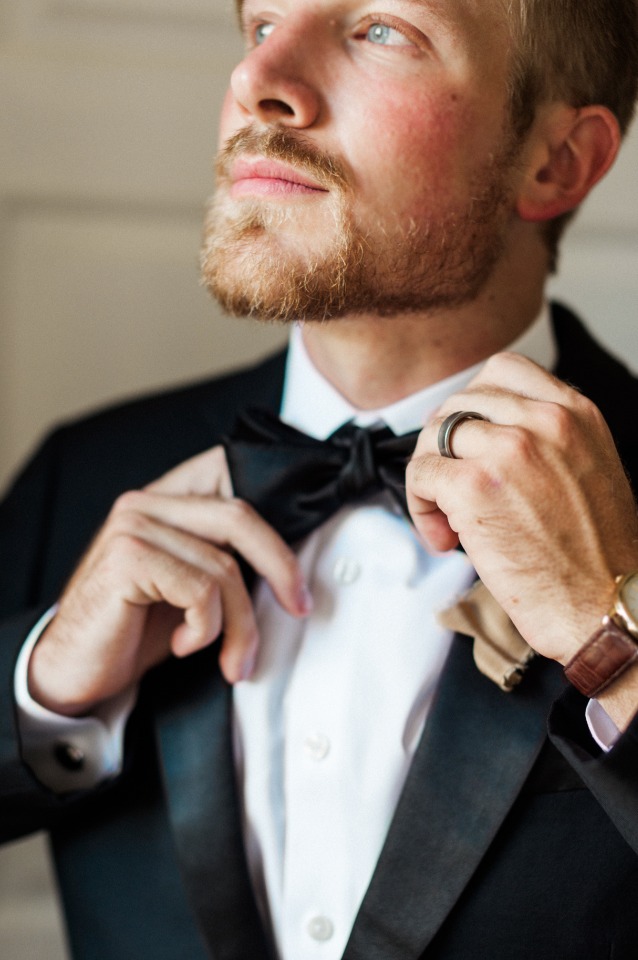 Groom adjusting his bow tie and looking up, ready for the big day