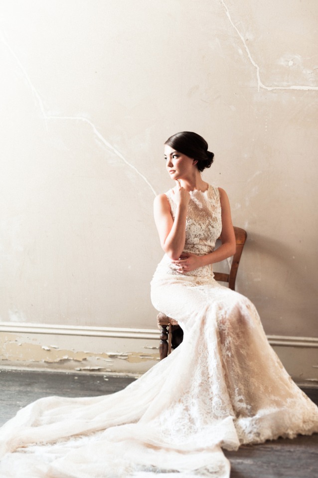 Bride in lace gown sits pensively on antique chair