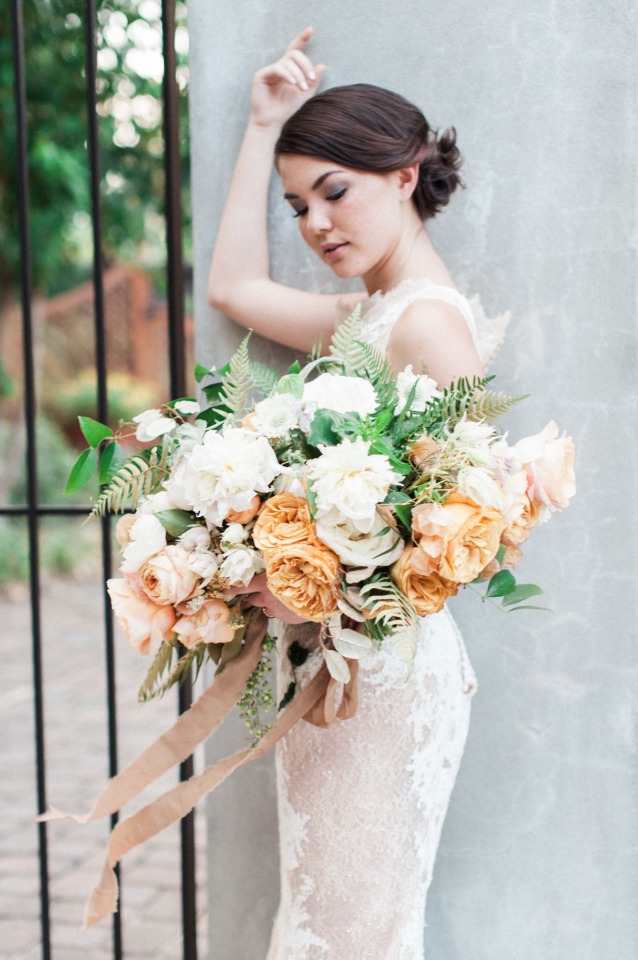 Elegant bride with bouquet and lace dress against a gray wall