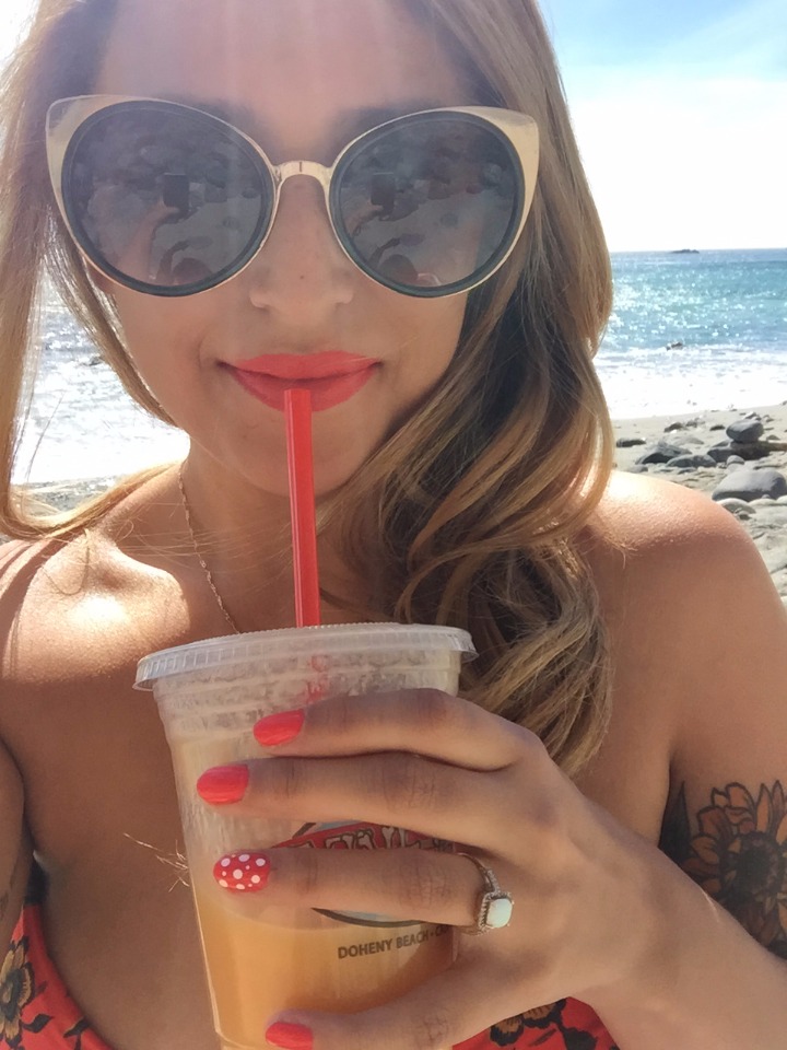 Woman enjoying a beach drink with red nails and cat eye sunglasses