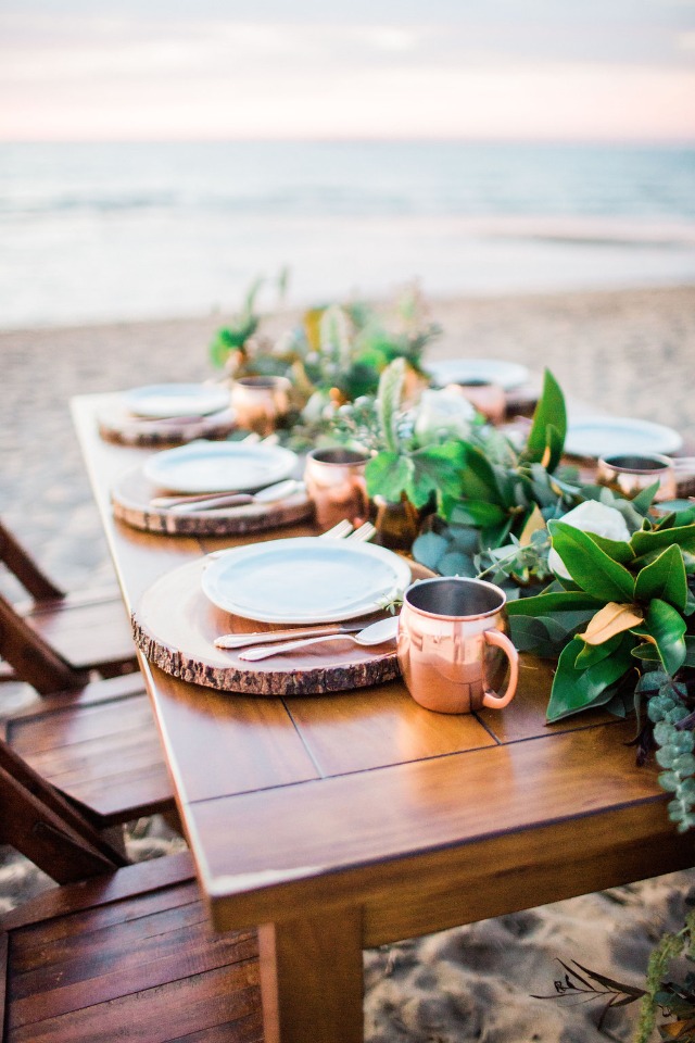 Elegant beach dining table with copper mugs and ocean