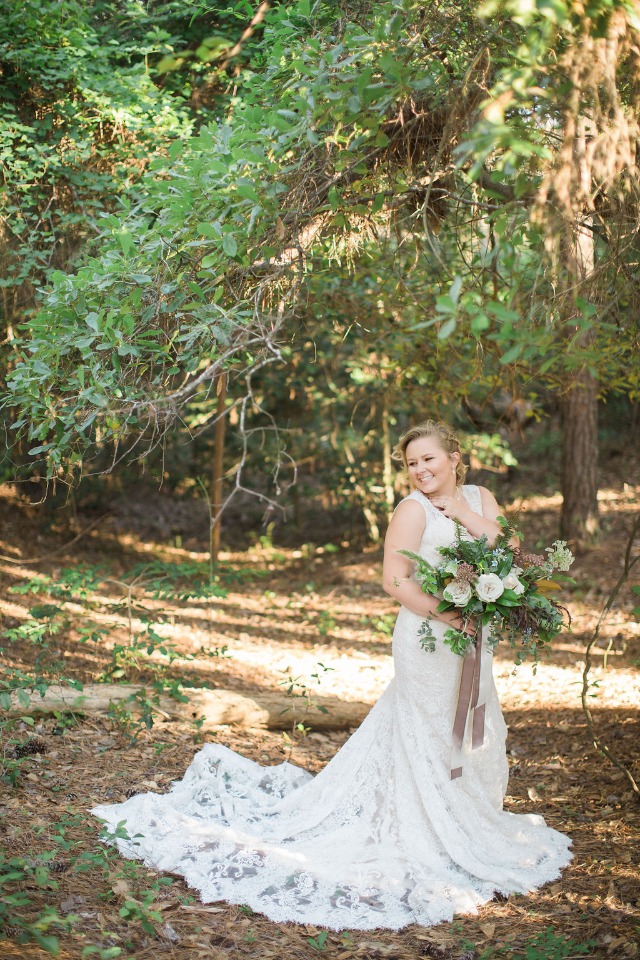 Bride in lace dress with bouquet in wooded landscape