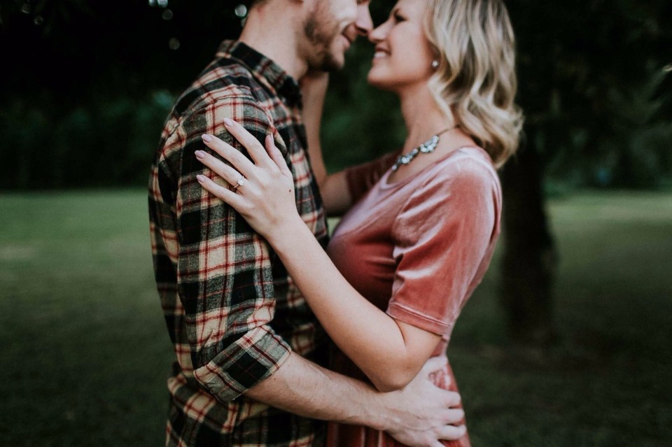 Engaged couple embracing outdoors, showing her ring