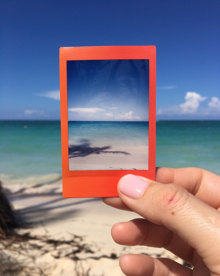Hand holding a polaroid photo of a beautiful beach scene
