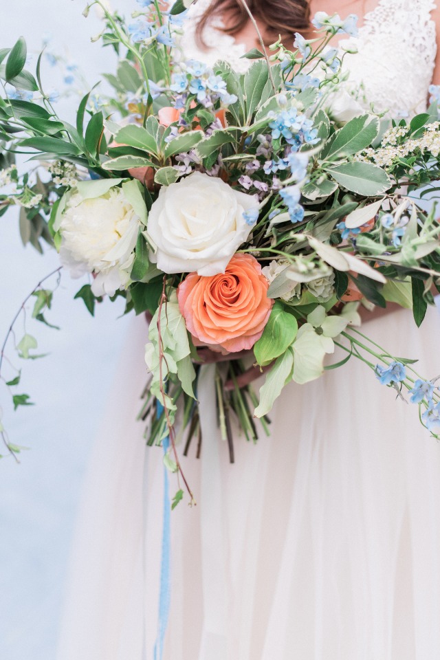 Bride holds a pastel rose and greenery wedding bouquet