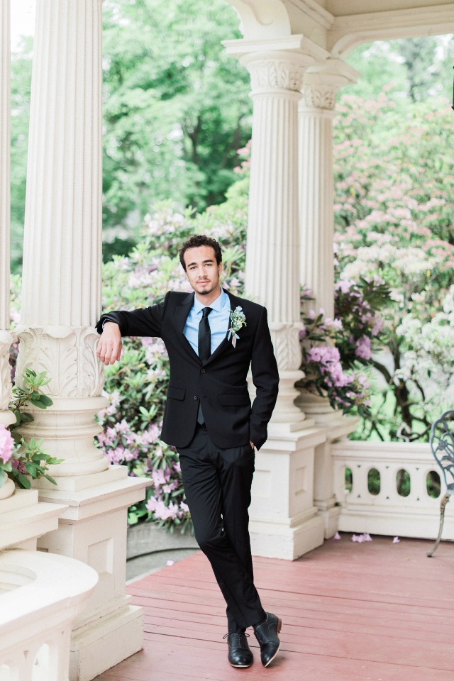 Groom in black suit poses at elegant outdoor venue