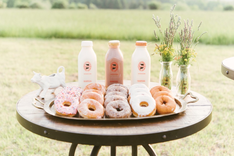 Fresh donuts and milk bottles on a wooden table outdoors