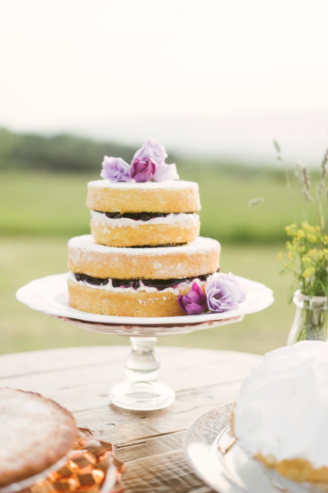 Two-tiered cake on a stand decorated with flowers, perfect for a garden party