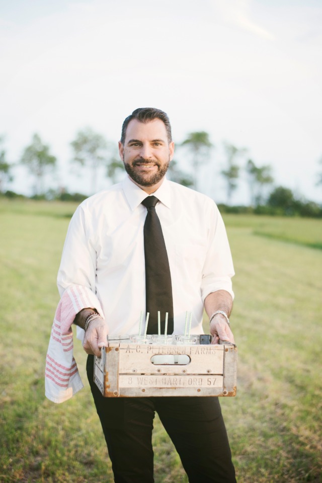 Man smiling and holding a crate of drinks outdoors in the field