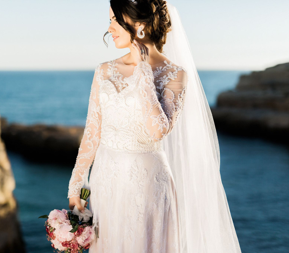 Bride in lace wedding dress holding bouquet by the sea