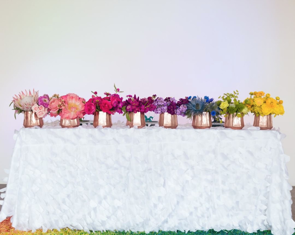 Colorful rainbow flowers in copper vases on white table cover