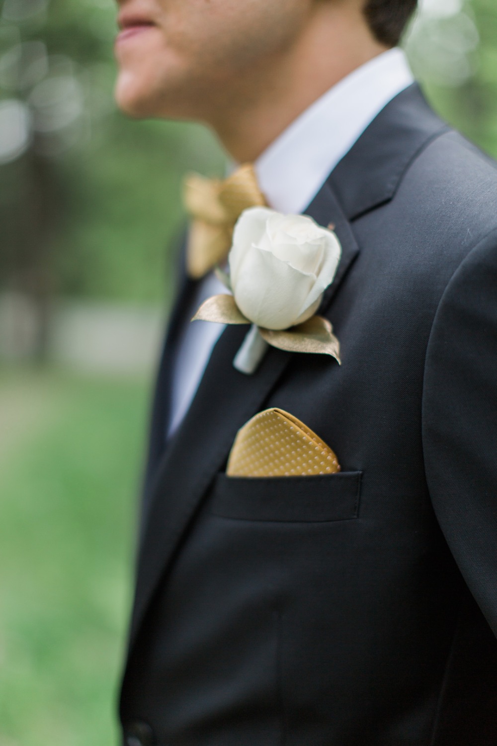 Groom in black suit with gold bow tie and white rose boutonniere
