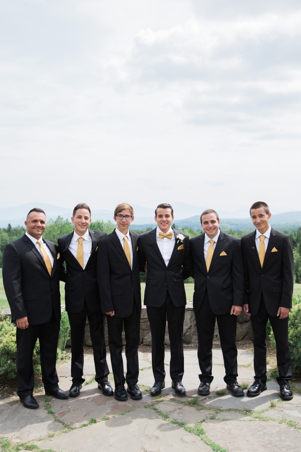 Groomsmen in black suits and gold ties pose outdoors