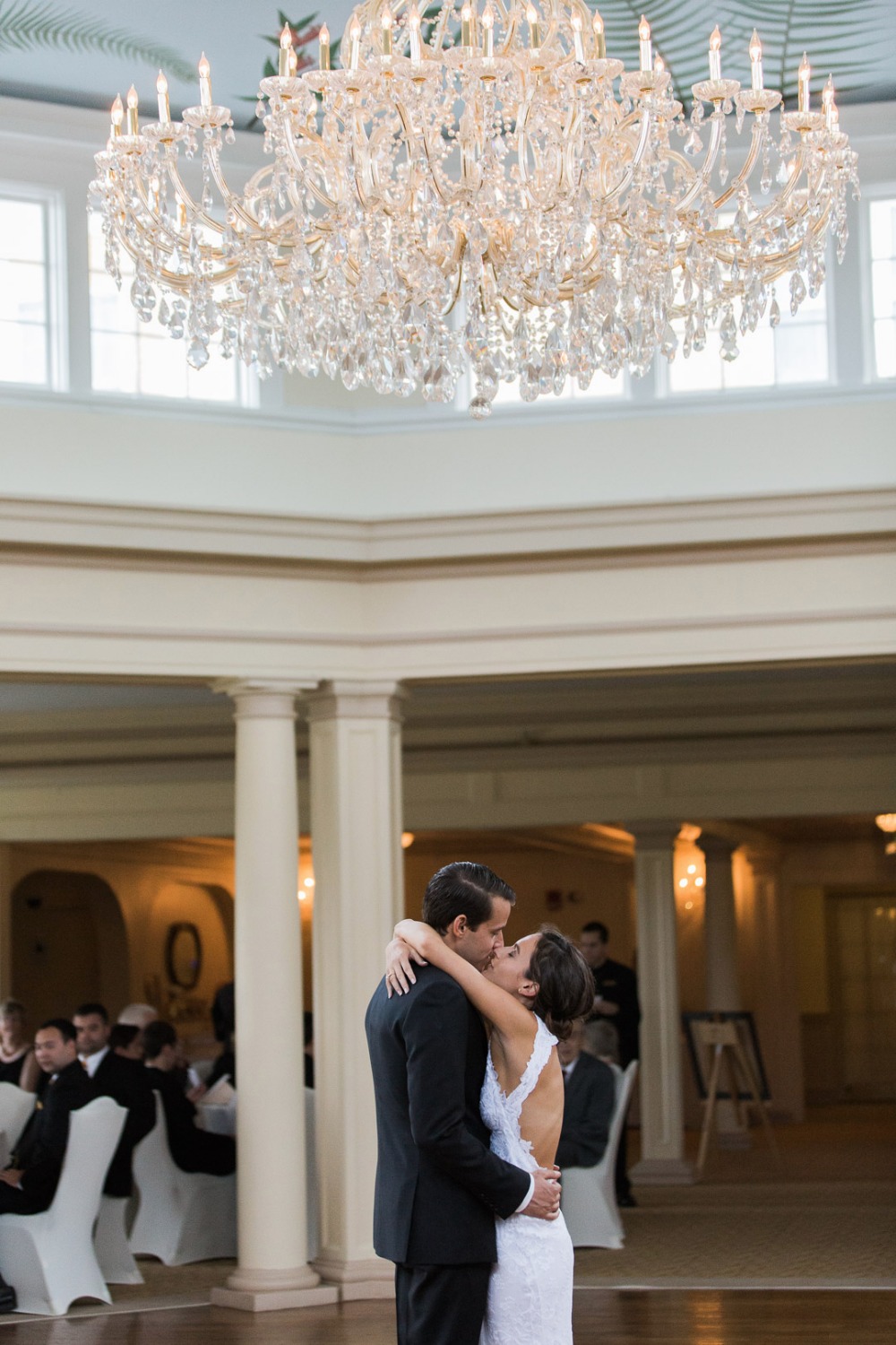 Newlyweds share a kiss under a sparkling chandelier at wedding reception