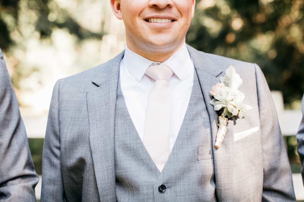 Groom in gray suit with boutonniere smiling at wedding