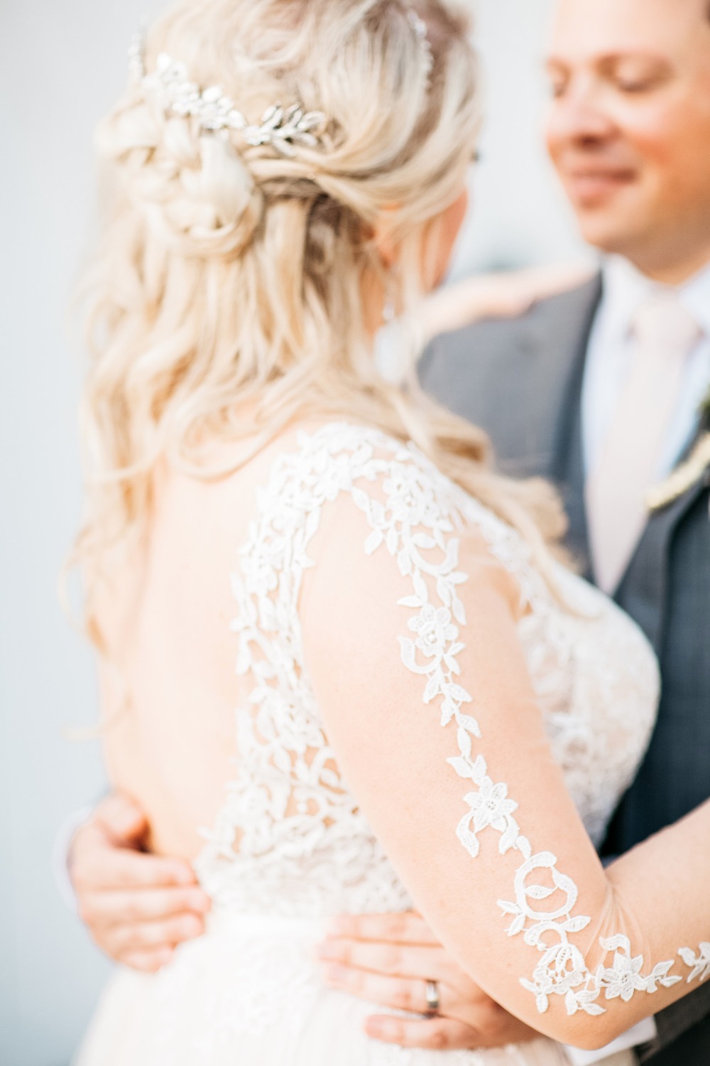 Bride embraces groom wearing lace sleeve wedding gown