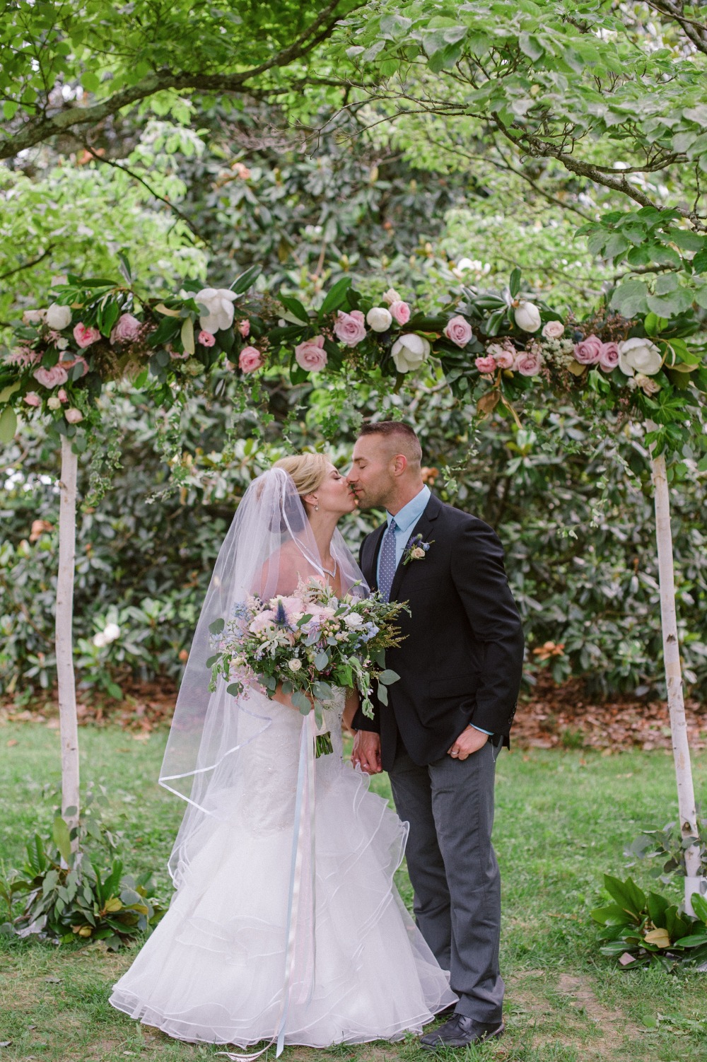 wedding kiss with floral accented wedding arch