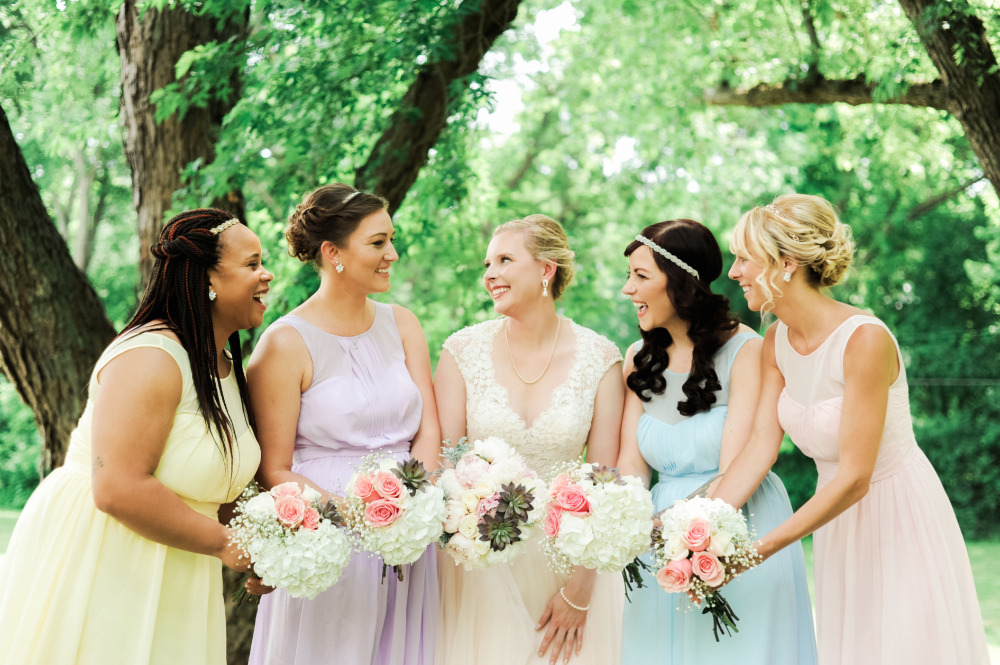 Bride and bridesmaids in pastel dresses smiling outdoors
