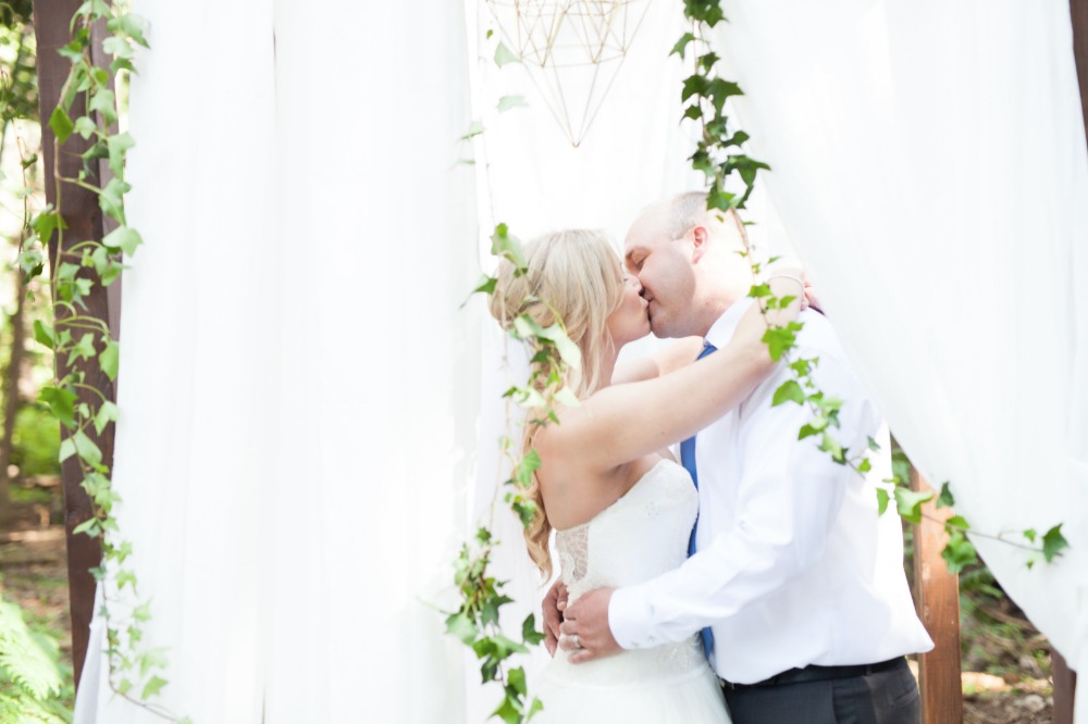 Newlyweds share a kiss at their ivy adorned wedding altar