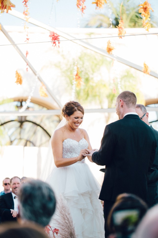 Bride smiles as groom puts on her ring during wedding ceremony