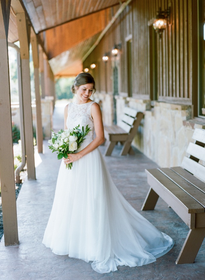 Smiling bride in white dress holding flowers outside