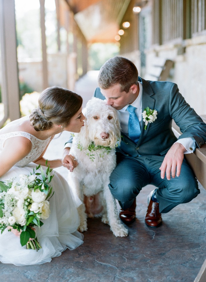 Bride and groom kissing their dog on their wedding day